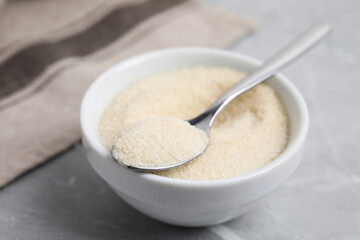 Gelatin powder in bowl and spoon on light grey marble table, closeup