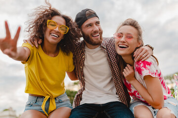 happy young company of smiling friends sitting in park