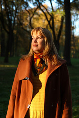 Portrait of middle aged Caucasian blonde woman in autumn park. Bright stylish woman in orange coat...