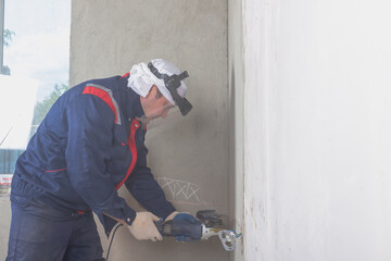 A worker cuts a groove in the wall with a grinder for installing electrical wiring