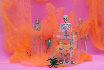 Orange pumpkin, skeletons, black spiders in a web on a pink background. Interior decoration for the Halloween holiday. A place to copy. Selective focus