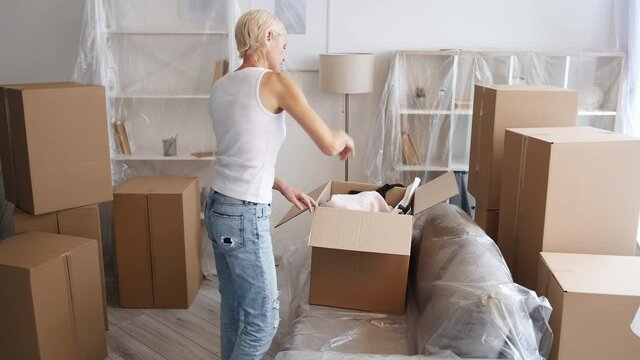 Relocation stress. Separation moving out. Property foreclosure. Annoyed mad mature woman packing stuff in carton boxes in light flat living room interior with isolated furniture.
