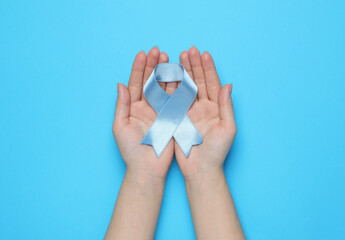 Woman holding light blue awareness ribbon on color background, top view