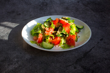 Salad of fresh vegetables with seeds. A white plate on a dark concrete background, illuminated by sunlight. The concept of vegetarian cuisine, raw food, diet. Close-up, top view, copy space