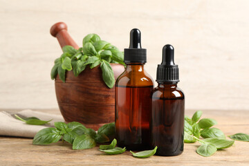 Bottles of basil essential oil near mortar with leaves and pestle on wooden table