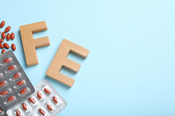 Wooden letters FE, pills and space for text on light blue background, flat lay. Anemia concept