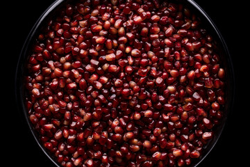 A lot of beautiful red pomegranate seeds in a black bowl