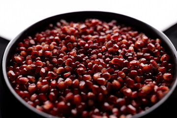A lot of beautiful red pomegranate seeds in a black bowl on a white background