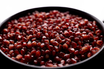 A lot of beautiful red pomegranate seeds in a black bowl on a white background
