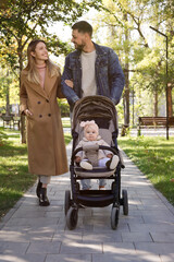 Happy parents walking with their baby in stroller at park on sunny day