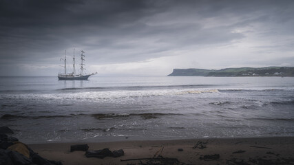 Dark, dramatic storm sky rolling over anchored tall ship near Northern Ireland coast with Fair Head in far distance, Ballycastle © Dawid
