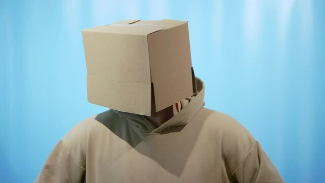A man with a box on his head depicts a robot on a blue background, a portrait of a man with a box on his head