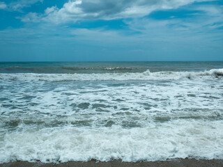 Fototapeta na wymiar Waves of the Sea Reaching the Shore with Lots of Foam in a Cloudy and Cold Sky
