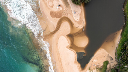 Aerial view of a river connected to an ocean on a beach in kauai, hawaii. Trees can be seen as well as waves and sand.
