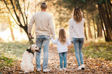 Fototapeta premium Happy beautiful family with dog labrador is having fun together walking the in park.