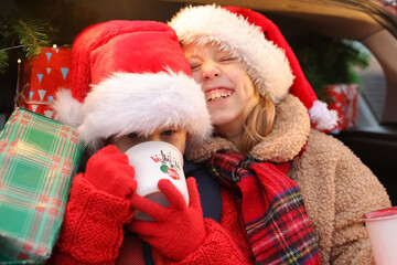 Fototapeta premium New Year's mood, brother and sister are sitting in a car full of gifts, children are having fun, rejoicing and choosing gifts