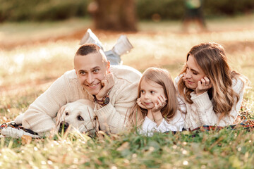 Fototapeta premium Happy family is having fun with dog labrador are lying on green grass in park.