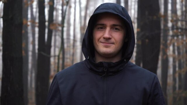 hooded man smiling while standing in the middle of the forest
