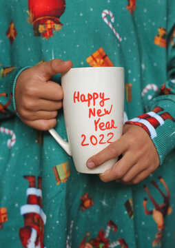 white mug with the inscription New Year 2022 in children's hands, the child is wearing a New Year's sweatshirt