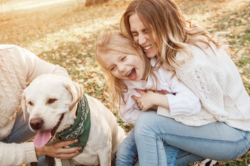 Happy beautiful family with dog labrador is having fun  are sitting on green grass in park.