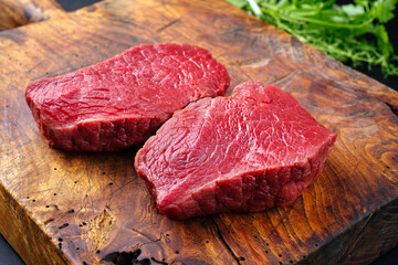 Raw dry aged bison beef rump steaks as top view with herbs on a rustic wooden board