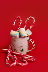 Christmas composition with hot chocolate decorated with marshmellows and candy canes isolated over red colored backgroud with copy space for ad