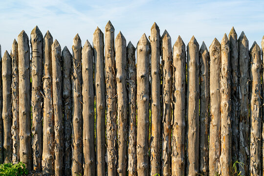 Wooden palisade made of logs. Log wooden fence. Sharp stakes in the ground.