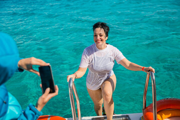 Happy woman in a wet T-shirt climbs stairs on board a boat after diving into the sea. Luxury travel...