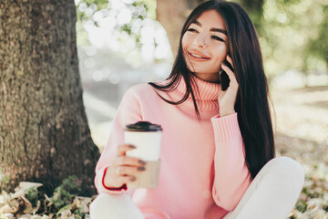 Beautiful woman drink coffee, using phone and sitting in the park.