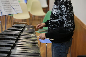 College student playing percussion musical instrument marimba on notes hitting black wooden keys with hammer stick in hand