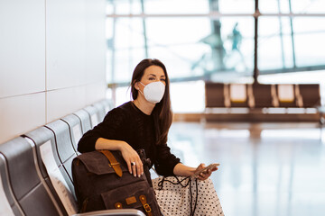 Tourist woman at the airport waiting for her flight. Wearing a mask for covid 19 protection using...