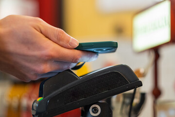A man's hand with a smartphone pays contactless payment through a terminal at the checkout in a cafe, close-up
