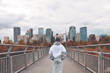 Young teenage girl from behind standing on bridge looking at city in front of her, Bow River Pathway