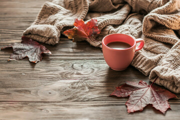Autumn morning coffee. A cup of coffee on a wooden table and a warm sweater on a background of autumn leaves. Still life concept. Copy space.