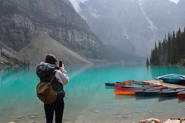 Young girl taking pictures of lake, canoes and mountains