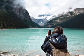Young girl taking pictures of lake and mountains