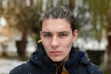 Portrait of a sad teen boy in winter in a warm coat but without a hat. The guy's hair on his head is tied in pigtails