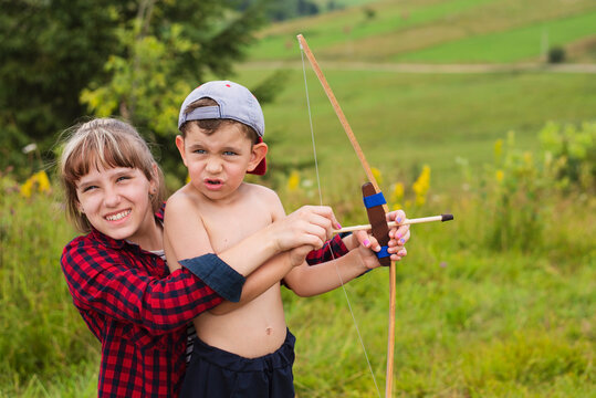 A little boy learns to shoot a bow in nature, next to him his older sister who teaches his brother to shoot, spends time with him, takes care of him