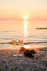 A romantic or Christmas evening on a sunny background. glare in the sea during sunset. Two glasses of champagne with grapes and shells. Vertical composition. Selective focus on glasses