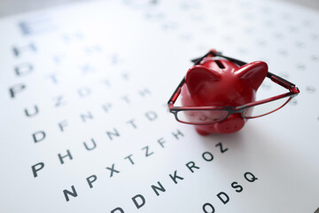 Red pig piggy bank in glasses stands on ophthalmological table closeup