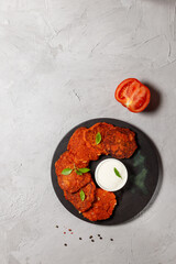 Greek tomato pancakes or cutlets on a black plate with sauce. Vertical frame on a gray background, top view, copy of the space