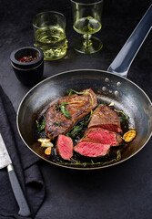 Traditional fried dry aged bison beef rump steaks with herbs and garlic served as close-up in a rustic metal skillet