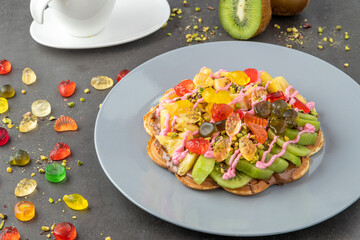Heart waffle with kiwi and pineapple with gummy candy and ice cream on it.