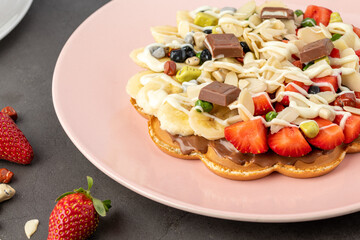 Heart waffle with banana and strawberry with gummy candy and ice cream on it.