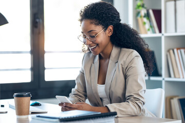 Elegant business woman sending messages with mobile phone while working in the office.