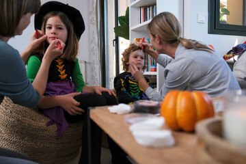 Sisters painting their daughters for halloween party.