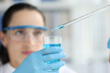 Female scientist dripping and pipetting into flask of blue liquid