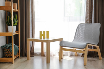 Table with decor elements near stylish armchair in interior of light living room
