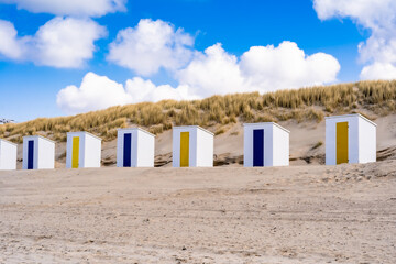 Obraz na płótnie Canvas Little beach cabins at a North Sea. White little houses on the deserted sand dunes of Netherlands with blue cloudy sky.