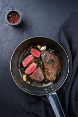 Traditional fried dry aged bison beef rump steaks with herbs and garlic served as top view in a...